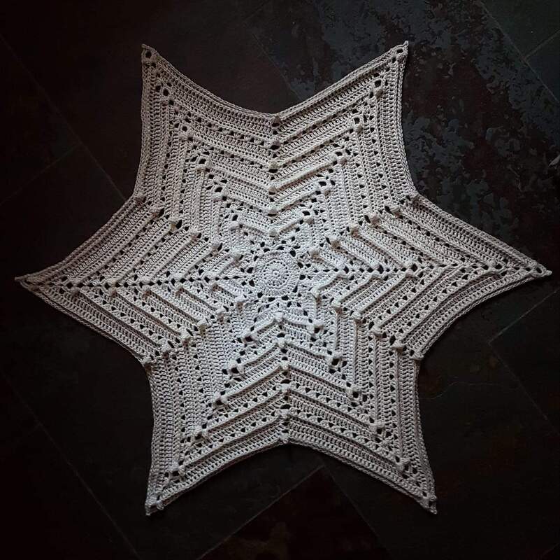 Weißes sternförmiges gehäkeltes Deckchen mit Loch- und Rippenmustern auf dunklem Untergrund