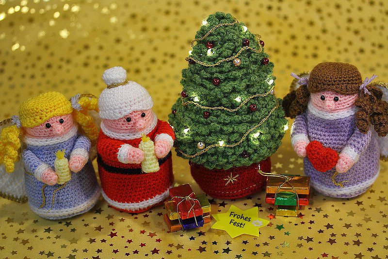 Gehäkelte Weihnachtsfiguren mit Tannenbaum, Weihnachtsmann, zwei Engeln und kleinen Geschenken vor goldenem Sternhintergrund
