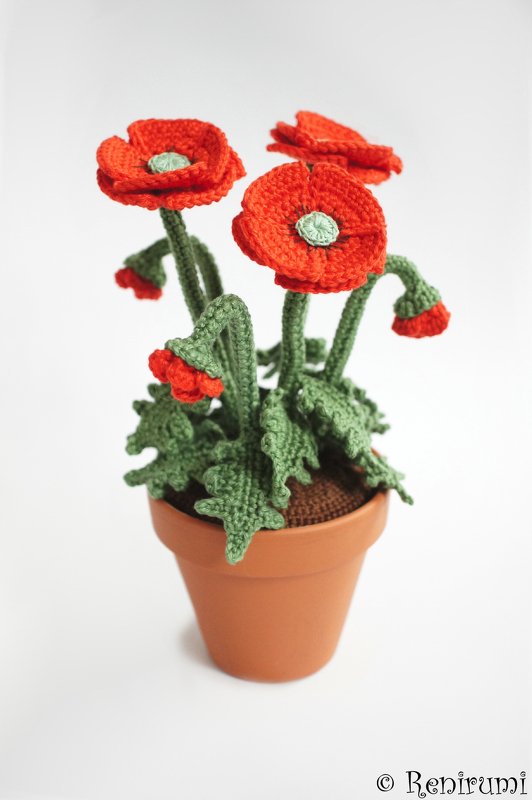 Crocheted red poppies and green leaves in a terracotta pot showing stitch detail for a pattern