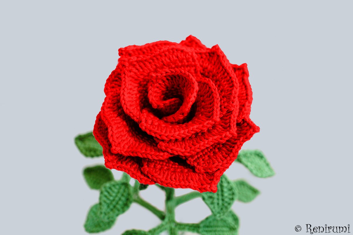 Kräftig rote gehäkelte Rose mit grünen Blättern