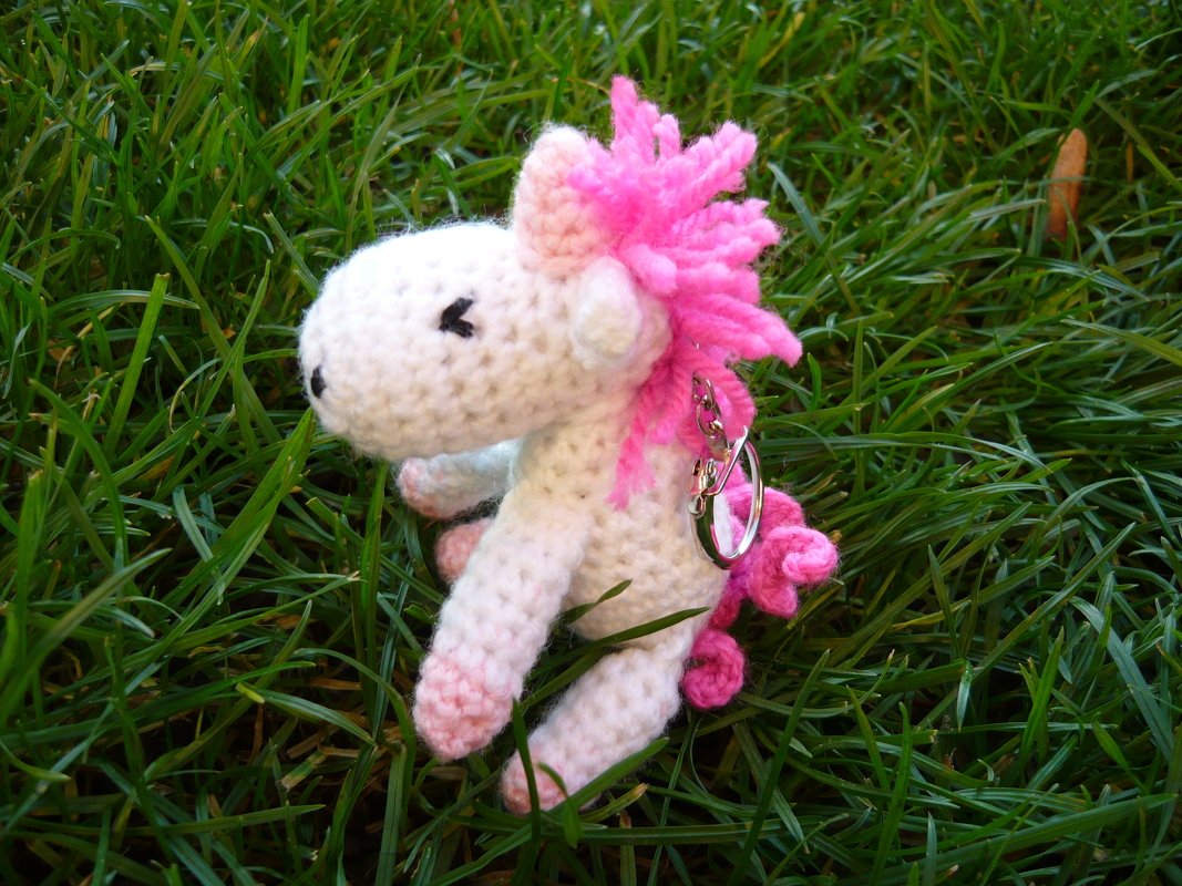 Gehäkelter weißer Einhorn-Schlüsselanhänger mit rosa Mähne im Gras