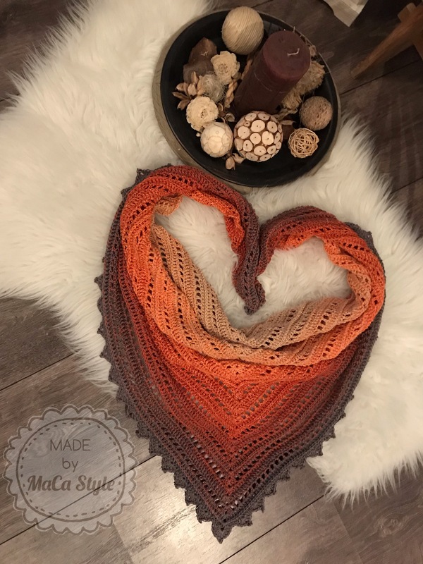Gehäkeltes Dreieckstuch in Orange- und Brauntönen mit Lochmuster und gezacktem Rand, herzförmig auf weißem Fell drapiert, Dekoschale mit Kerze daneben