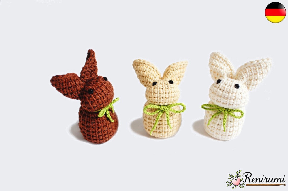 Drei gehäkelte Amigurumi-Hasen in Braun, Beige und Creme mit grünen Schleifen