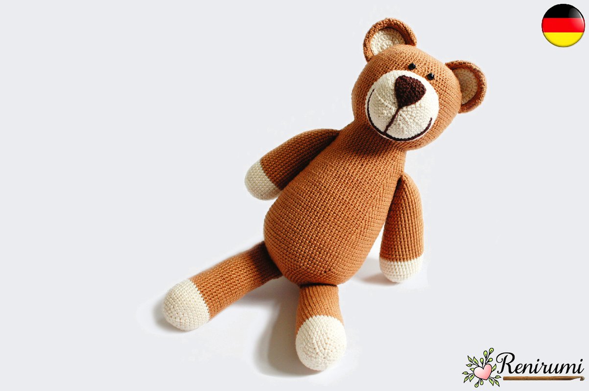 Brauner Amigurumi-Teddy mit cremefarbenen Pfoten und lächelnder Schnauze, liegend