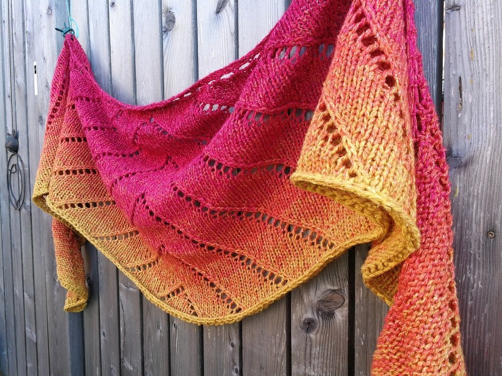 Gestricktes Dreieckstuch mit Gelb–Orange–Rotem Farbverlauf an Holzzaun
