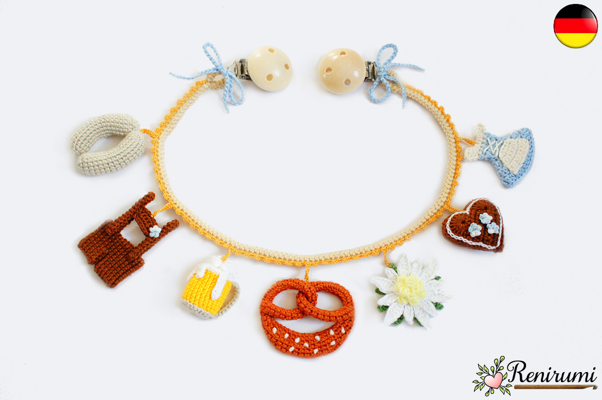 Handgehäkelte Schnullerkette mit bayerischen Anhängern (Brezel, Maßkrug, Edelweiß, Herz) an beige-orangefarbener Kordel und zwei Holzclips.