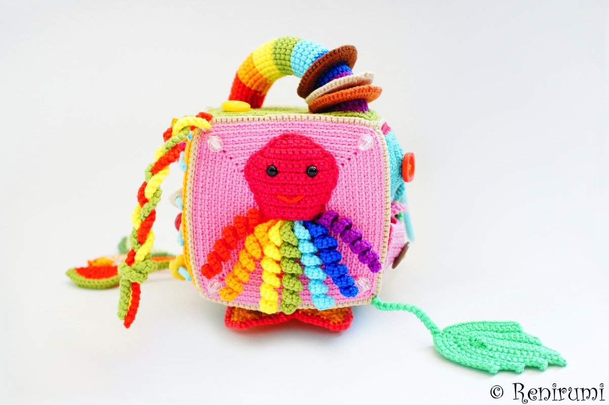 Multicolored crocheted baby activity cube with rainbow octopus, rings, braided cord and buttons.