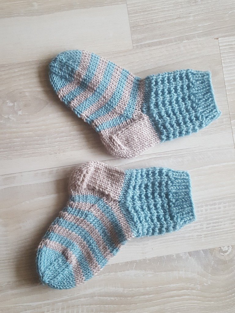 Paar gestrickter Babysocken in Blau und Beige mit Streifen und strukturiertem Bündchen auf hellem Holz
