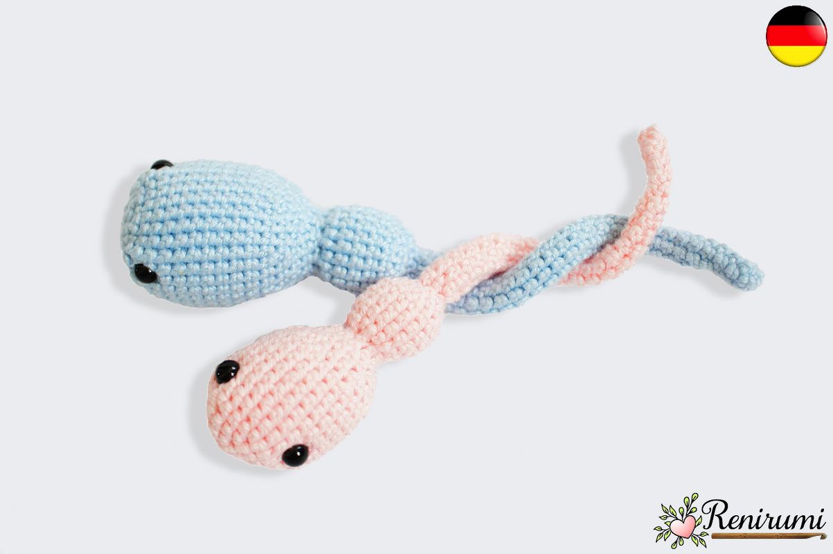 Zwei ineinander verschlungene gehäkelte Amigurumi-Figuren in Hellblau und Zartrosa vor hellem Hintergrund.