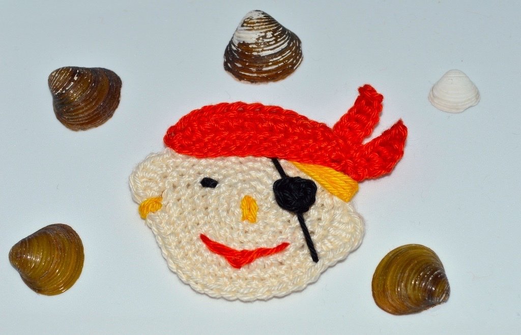 Bunt gehäkelter Piratenkopf mit rotem Kopftuch und schwarzer Augenklappe, dekorativ präsentiert