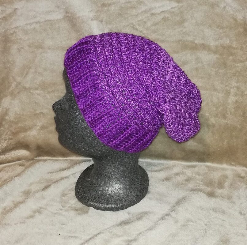 Lila gehäkelte Beanie auf dunklem Mannequinkopf vor hellem, strukturiertem Hintergrund