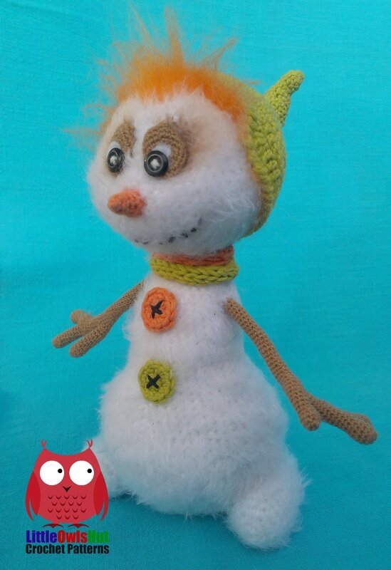 Fuzzy crocheted amigurumi snowman with spiky orange hair, pointed green hat, striped scarf, button accents and crocheted arms on a blue background.
