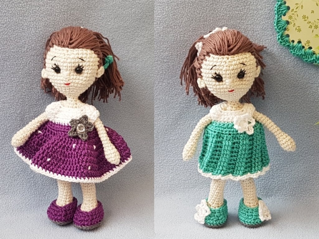Zwei gehäkelte Amigurumi-Puppen mit braunen Haaren, eine im lila Kleid mit Blume, eine im grünen Kleid mit weißer Blüte