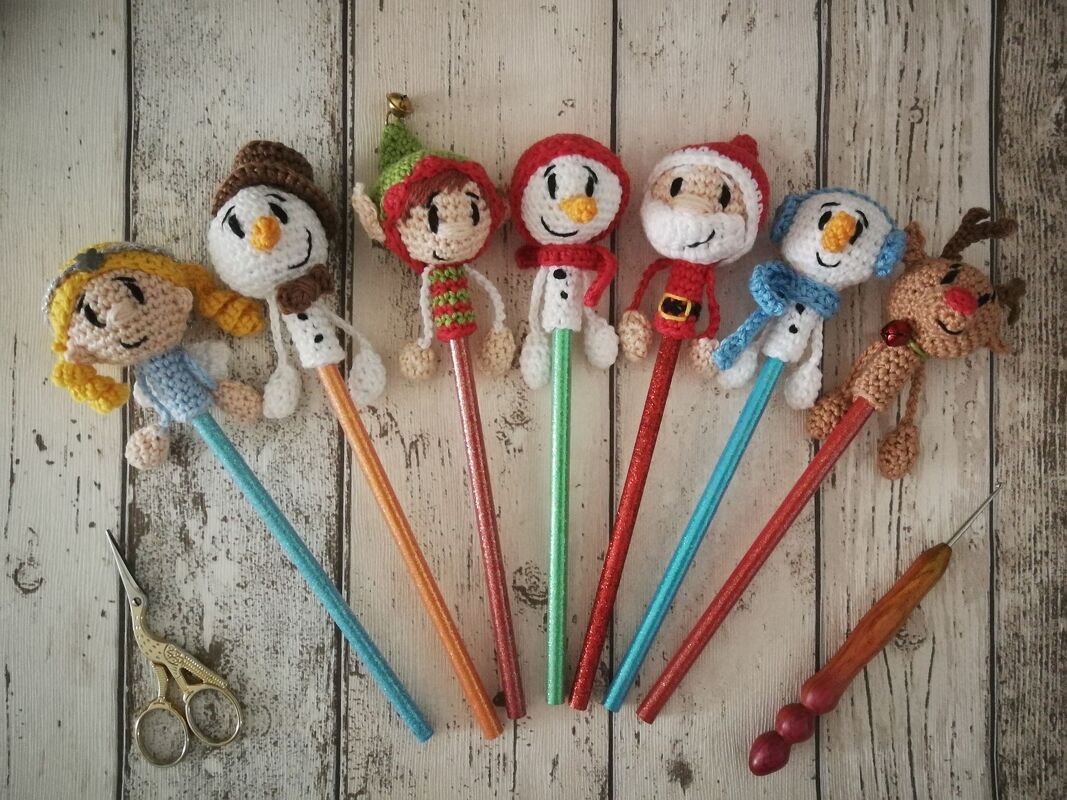 Reihe gehäkelter Weihnachts-Stiftaufsätze auf Holzuntergrund