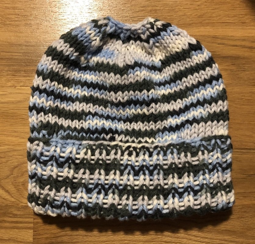 Gestrickte Damenmütze mit Streifen in Blau, Grau und Weiß auf Holzuntergrund