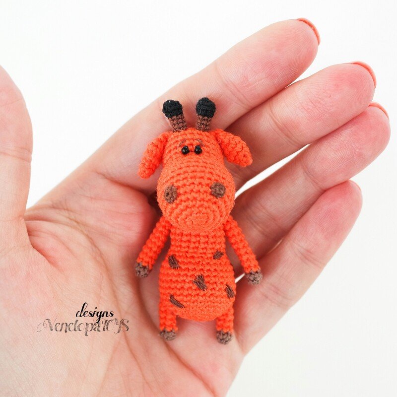 Tiny orange amigurumi giraffe with brown spots held in an open hand