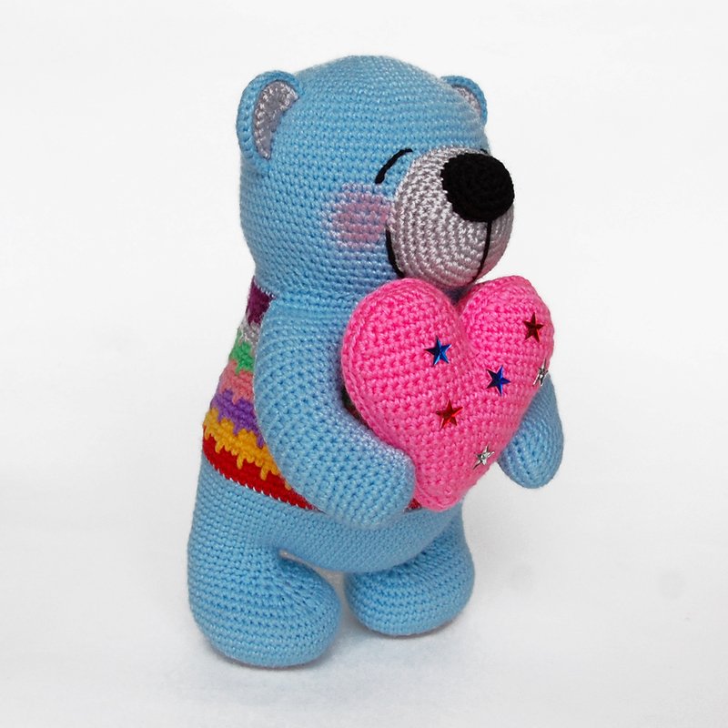 Crocheted blue teddy bear hugging a pink heart embellished with star sequins