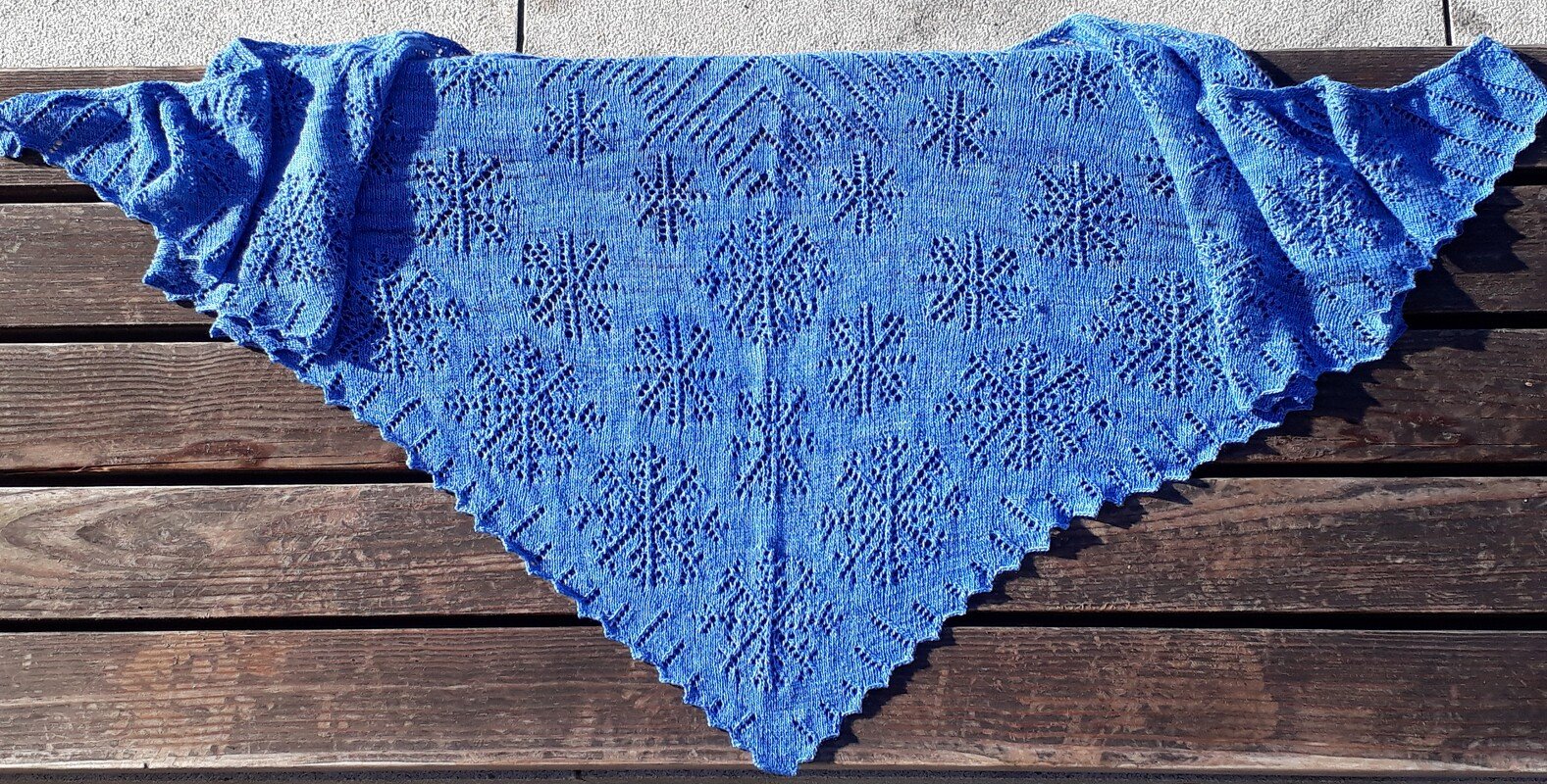 Gestricktes blaues Dreieckstuch mit filigranem Ajourmuster auf Holz