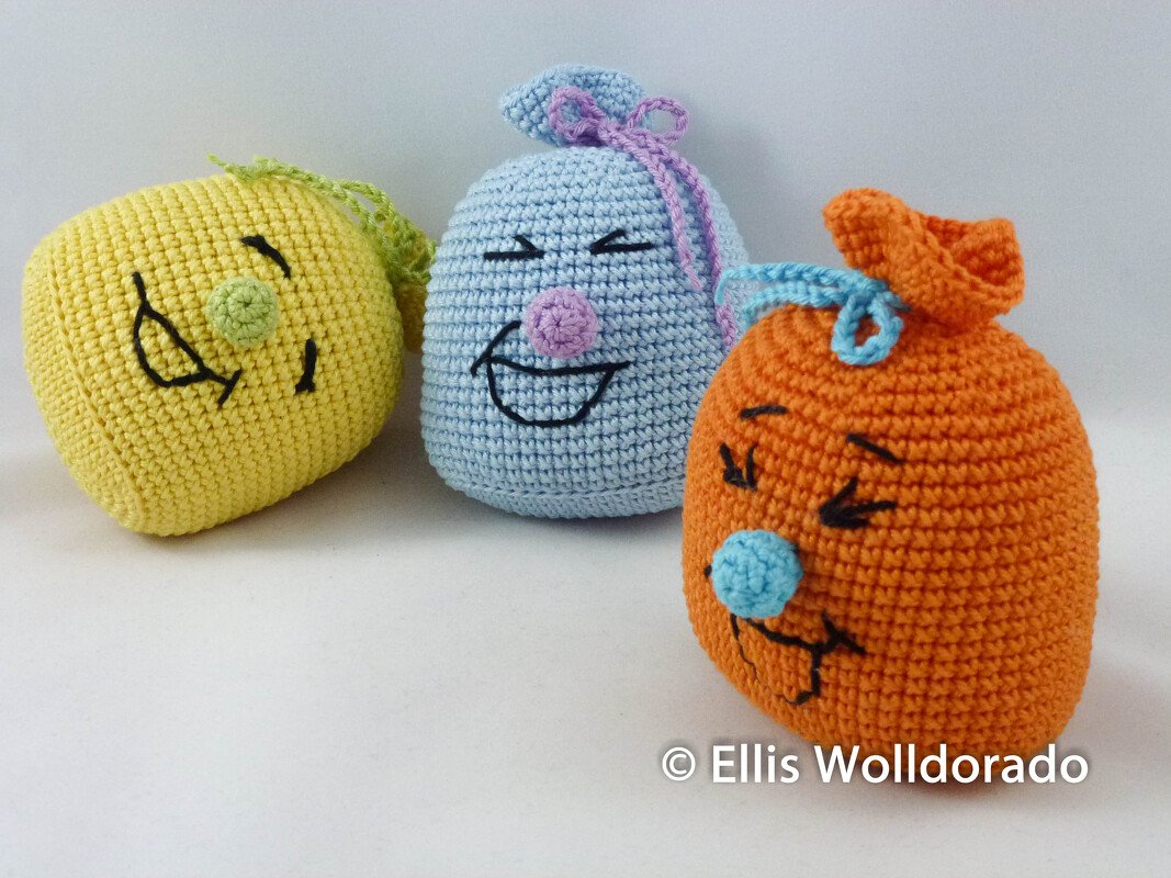 Drei gehäkelte Amigurumi-Beutel in Gelb, Hellblau und Orange mit gestickten Gesichtern und Zugbändern