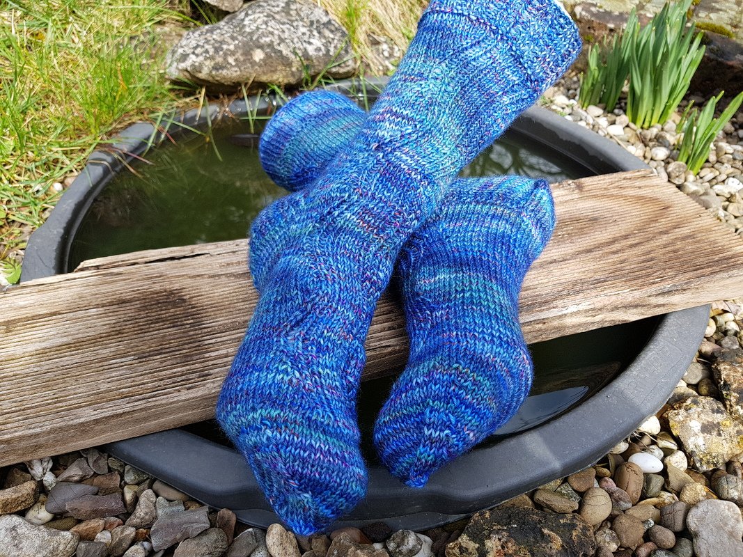 Melierte blaue handgestrickte Damensocken mit Strukturmuster auf Holzbrett über einem Wasserbecken