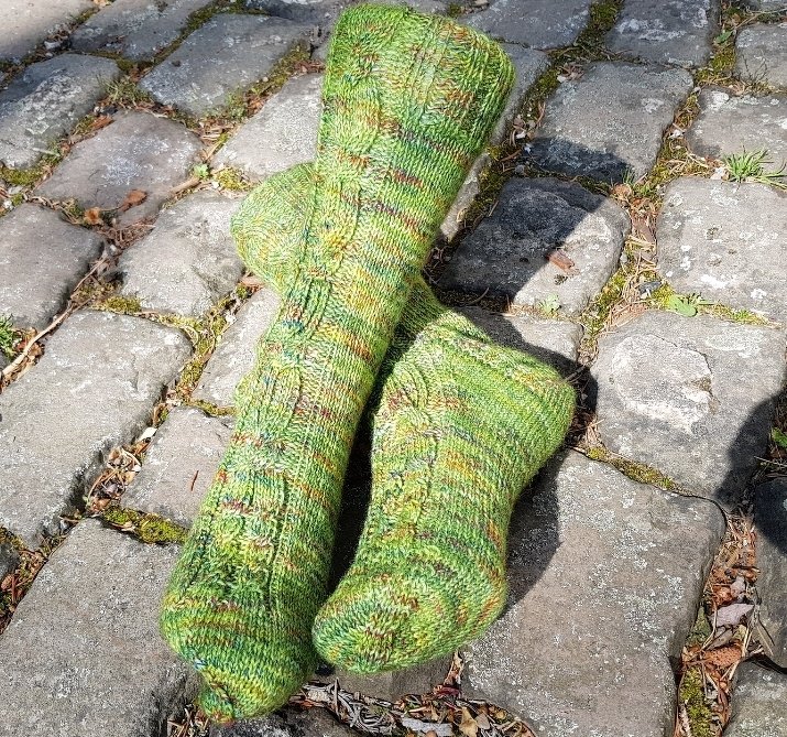 Handgestrickte grüne Damensocken mit Zopfmuster auf Pflastersteinen