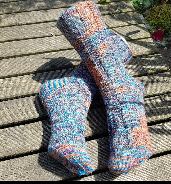 Handgestrickte mehrfarbige Socken mit Rippbündchen auf Holzplanken.