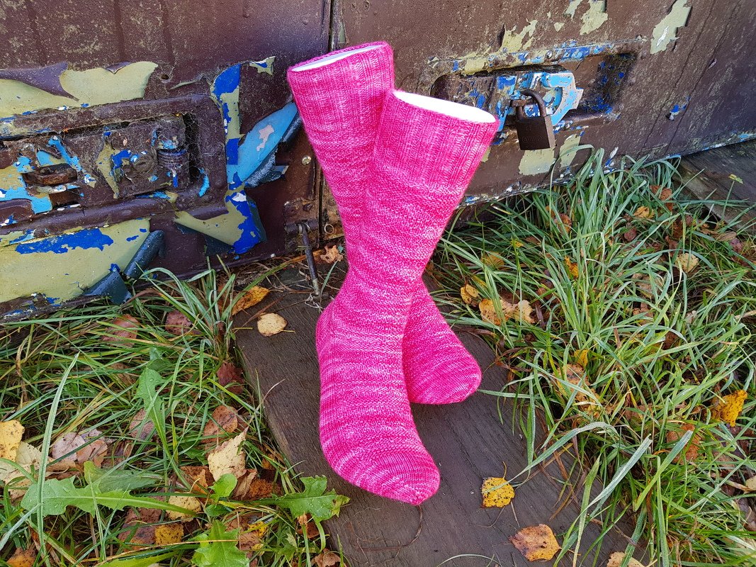 Handgestrickte wadenhohe Herrensocken in kräftigem Rosa auf Holz vor verwitterter Metalltür