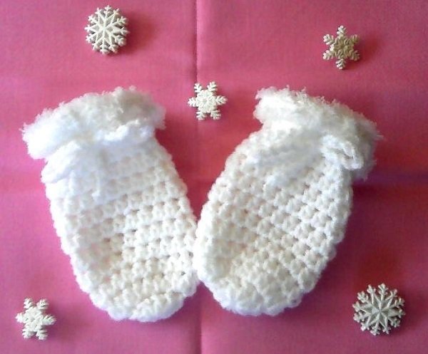 Weiße gehäkelte Babyfäustlinge mit flauschigem Bündchen auf rosa Hintergrund und Schneeflocken-Dekor