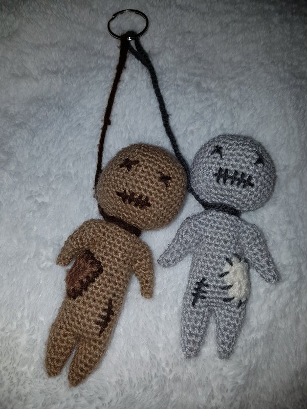 Zwei handgehäkelte Amigurumi-Püppchen als Schlüsselanhänger, braun und grau, mit gestickten Nähten und Flicken