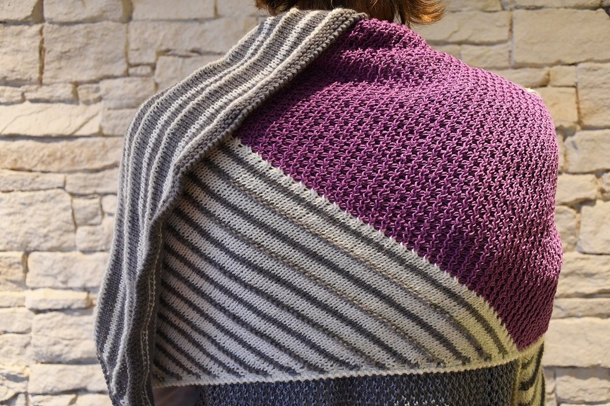 Rückenansicht eines gestrickten Dreieckstuchs mit violettem Strukturteil und diagonal verlaufenden grau-weißen Streifen