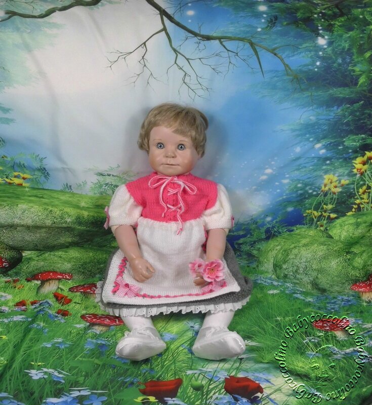 Gestricktes Babykleid an einer Puppe in Rosa, Weiß und Grau vor einem fantasievollen Hintergrund