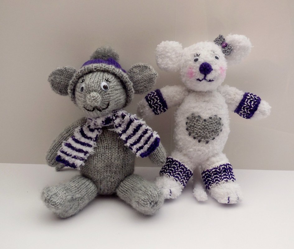 Zwei Amigurumi-Figuren: graue Maus mit Mütze und Schal, weißes Fantasietier mit Herz und gemusterten Bündchen.