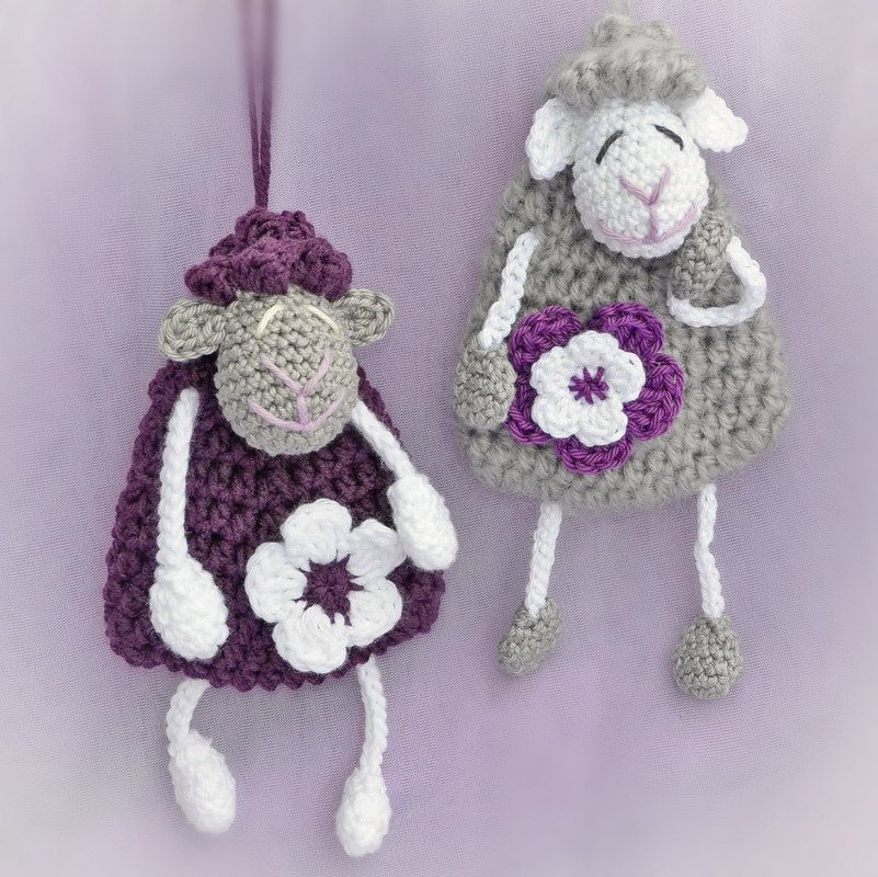 Zwei gehäkelte Schäfchen-Anhänger in lila und grau mit weißen Blumen
