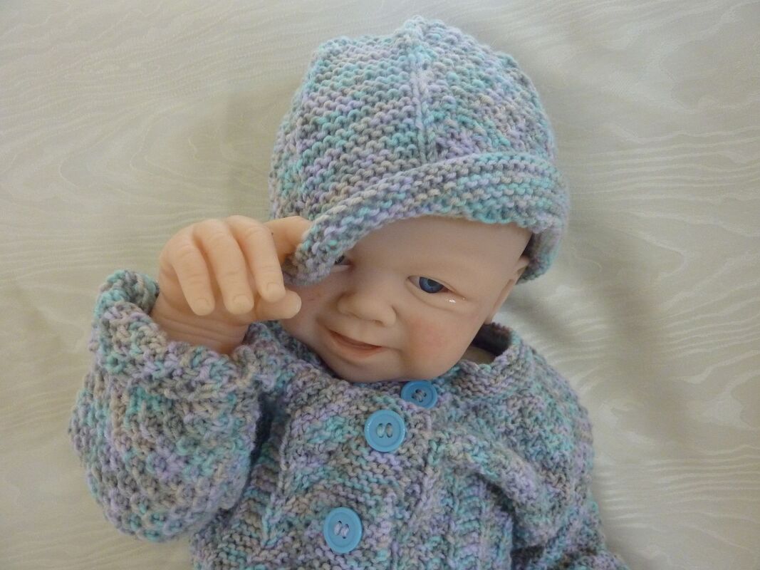 Babypuppe mit handgestrickter Mütze und Jacke in Pastellfarben mit blauen Knöpfen.