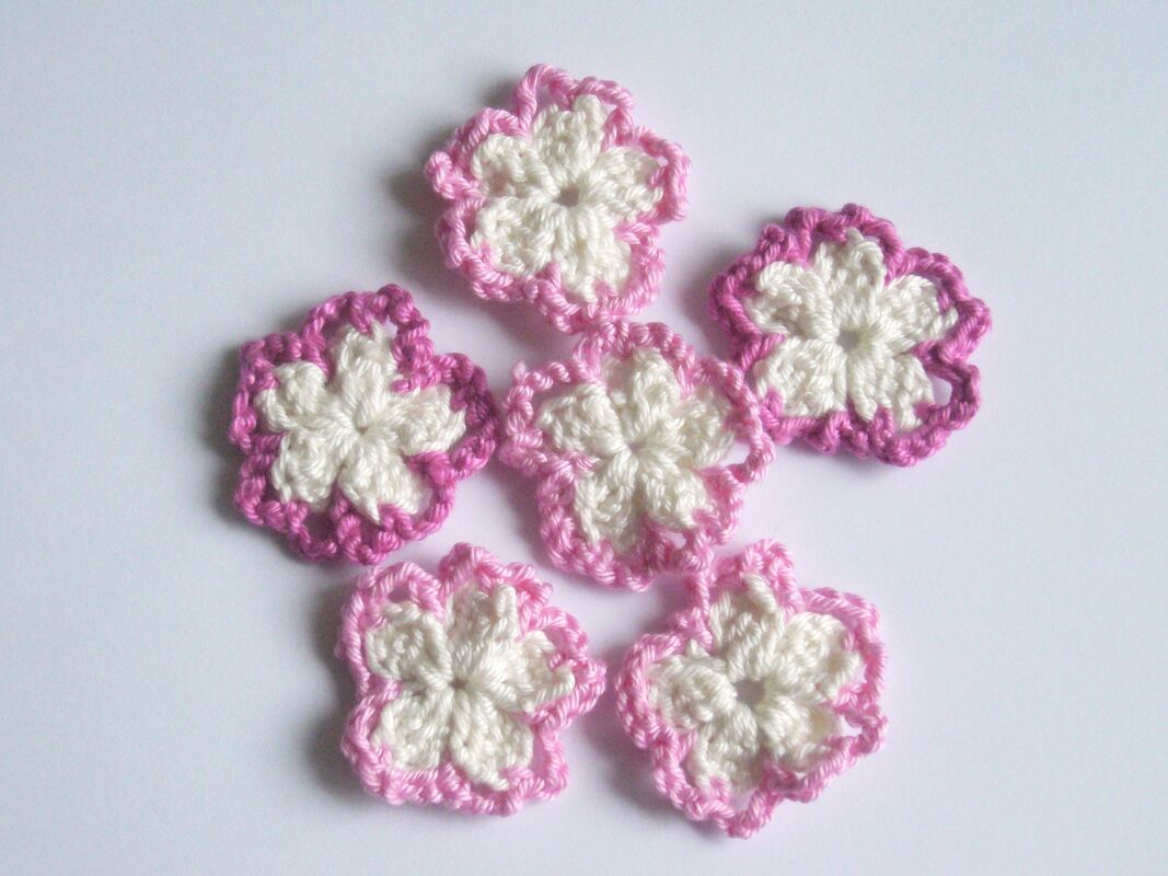 Sechs gehäkelte Blumen-Applikationen in Rosa und Weiß auf hellem Hintergrund