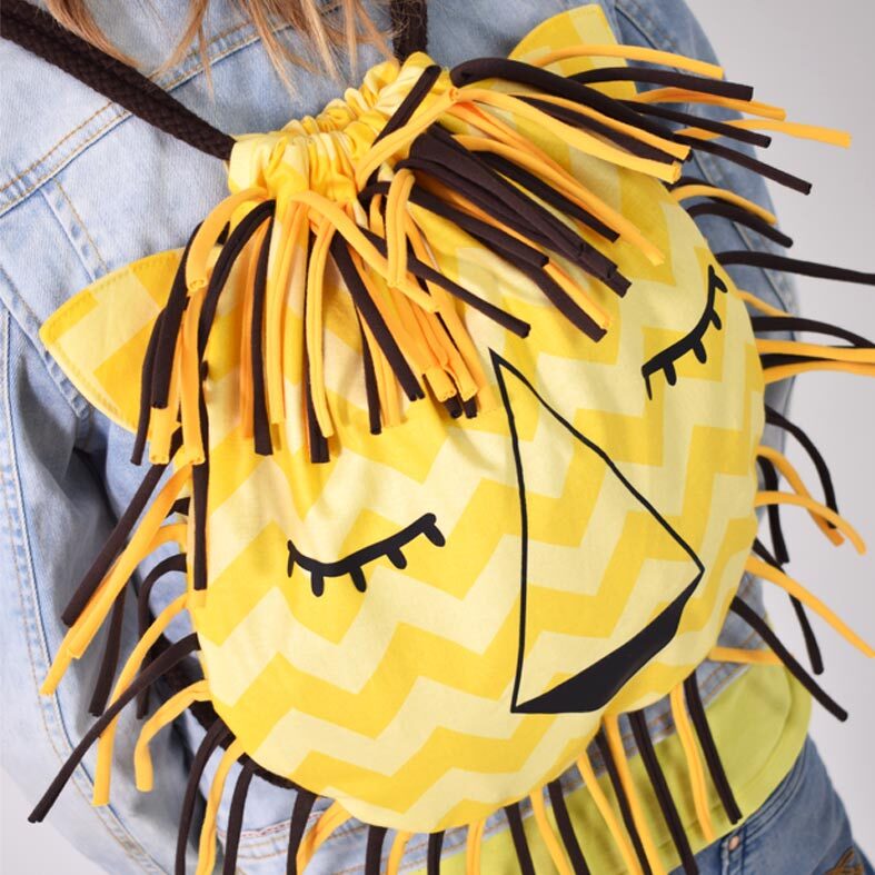 Gelber Löwenbeutel mit Zickzack-Muster, Fransenmähne und geschlossenen Augen, getragen auf dem Rücken