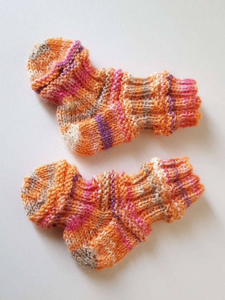Bunte handgestrickte Babysocken in Orange, Pink und Lila auf weißem Hintergrund.