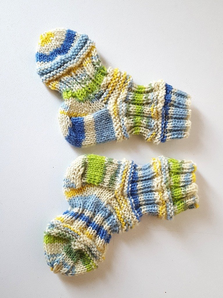Zwei gestrickte Babysocken mit blauen, grünen und gelben Streifen auf hellem Untergrund