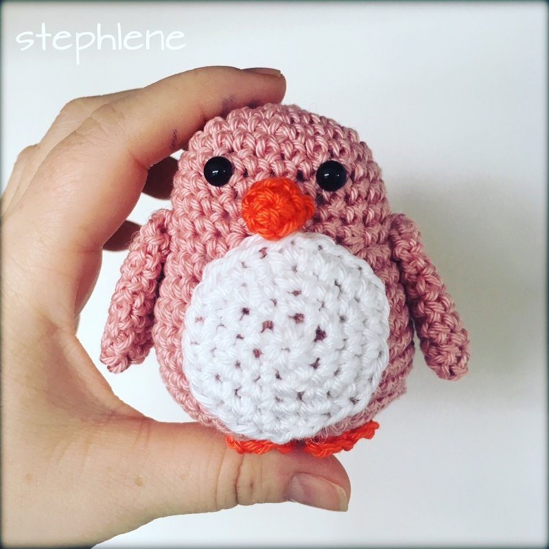 Hand hält kleines gehäkeltes Amigurumi-Vogelchen in Rosa mit weißem Bauch und orangefarbenem Schnabel