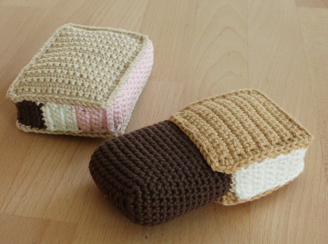 Zwei gehäkelte Eisriegel in Beige, Braun und Rosa auf Holzuntergrund