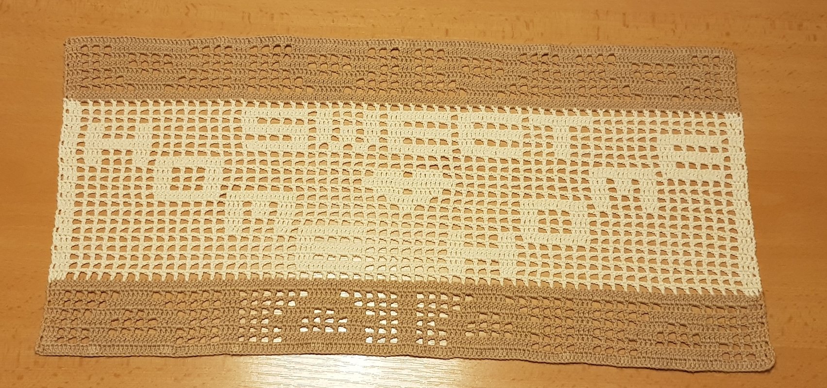 Gehäkelter rechteckiger Tischläufer in Creme und Beige mit Filetmuster und Schriftzug auf Holztisch