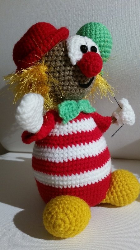 Gehäkelter Clown-Amigurumi mit rot-weiß gestreiftem Körper, roter Mütze und gelben Füßen