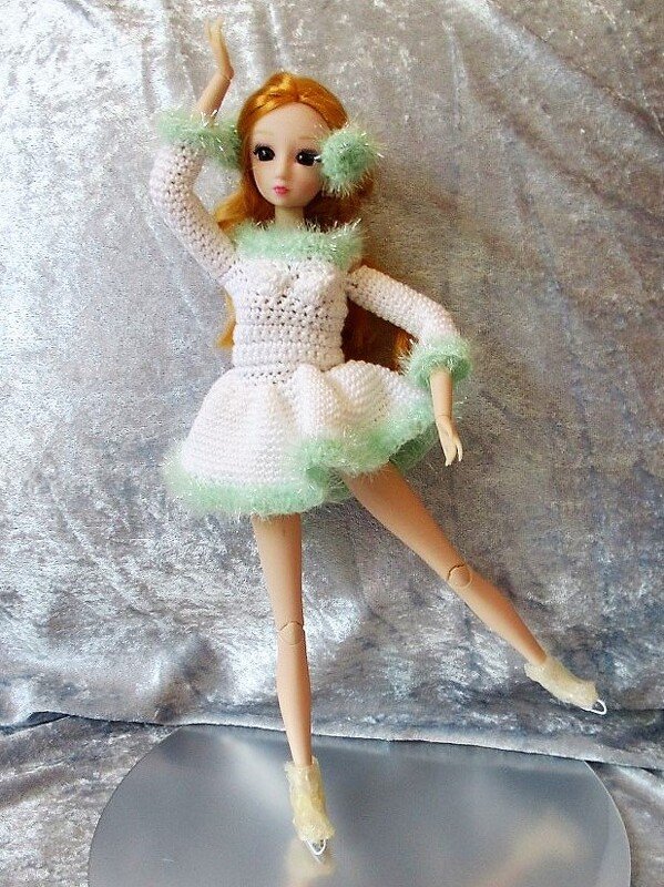 Puppe mit rotem Haar in gehäkeltem weißen Eiskunstlaufkleid mit mintgrünem Flauschbesatz und Schlittschuhen.