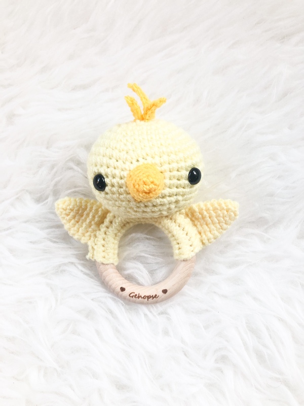 Gehäkelter gelber Küken-Beißring mit rundem Holzring auf weißem Plüsch