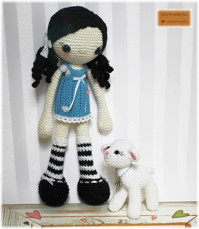 Amigurumi-Puppe mit schwarzen Zöpfen und blauem Kleid neben weißem Lamm
