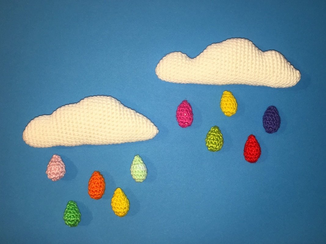 Zwei weiße gehäkelte Wolken mit bunten gehäkelten Regentropfen vor blauem Hintergrund