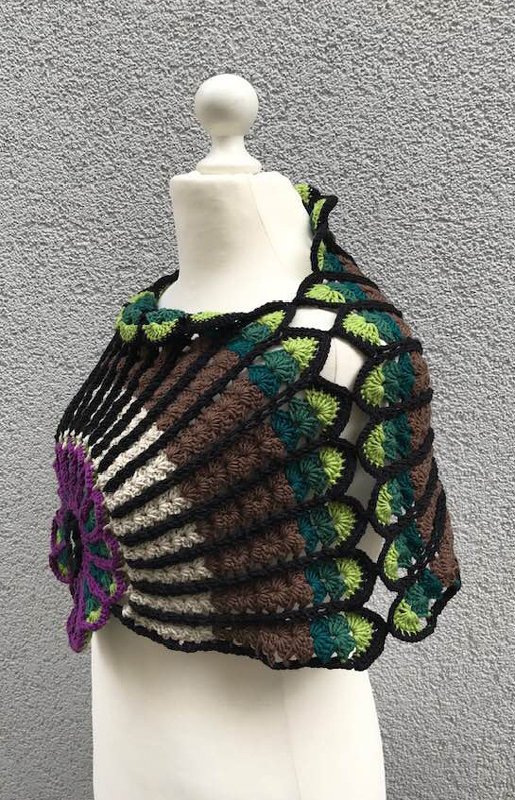 Schaufensterpuppe mit gehäkeltem Poncho: braune und grüne Fächerreihen, schwarze Netzkante und lila Blütenapplikation