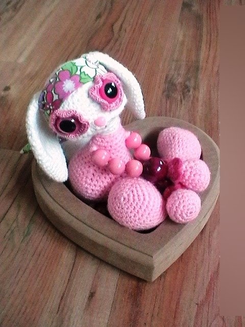 Gehäkelter Amigurumi-Hase in Weiß und Rosa mit Blumenstirnband in herzförmiger Holzschale