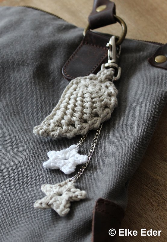 Crocheted angel wing and star keychain clipped to a grey bag