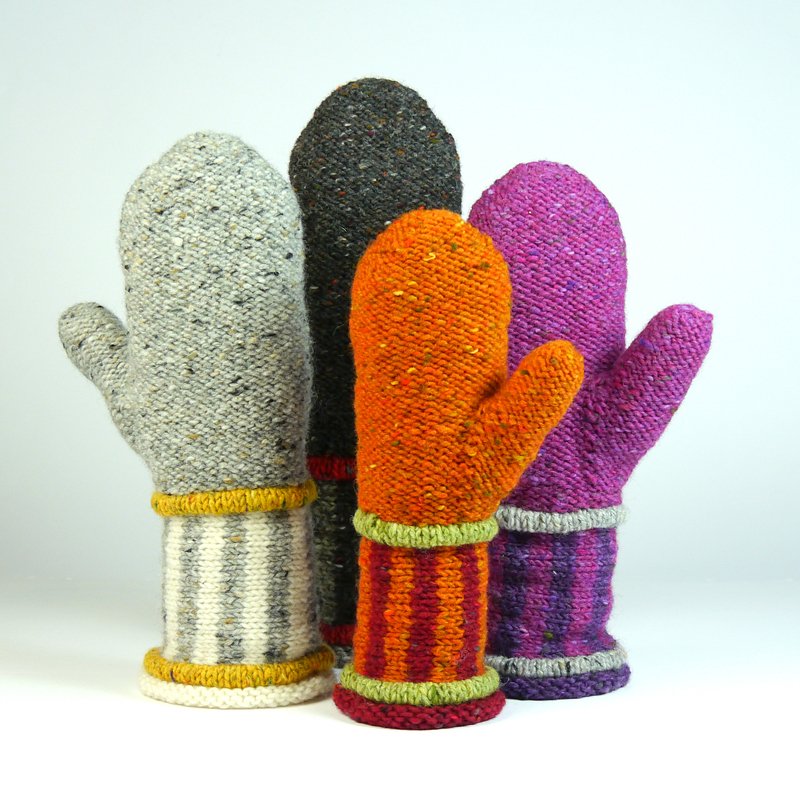Four hand-knitted mittens in light grey, dark grey, orange, and purple with contrasting ribbed or striped cuffs, standing upright on a white background.